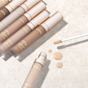 Universal Concealer in diverse shades featuring a creamy liquid texture and applicator on a stone background.