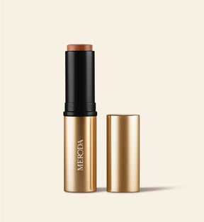 Soft Tan Bronzer stick in shade Dark shown upright with its gold cap placed neatly beside it.
