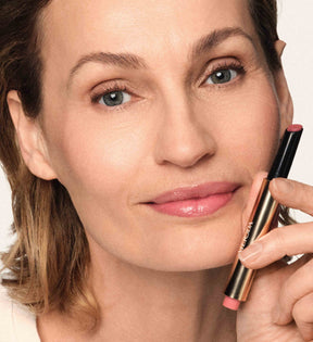 Model holding the Hydrating Lip Tint in Dusty Rose near her face, showcasing glossy pink lips and a fresh natural makeup look.