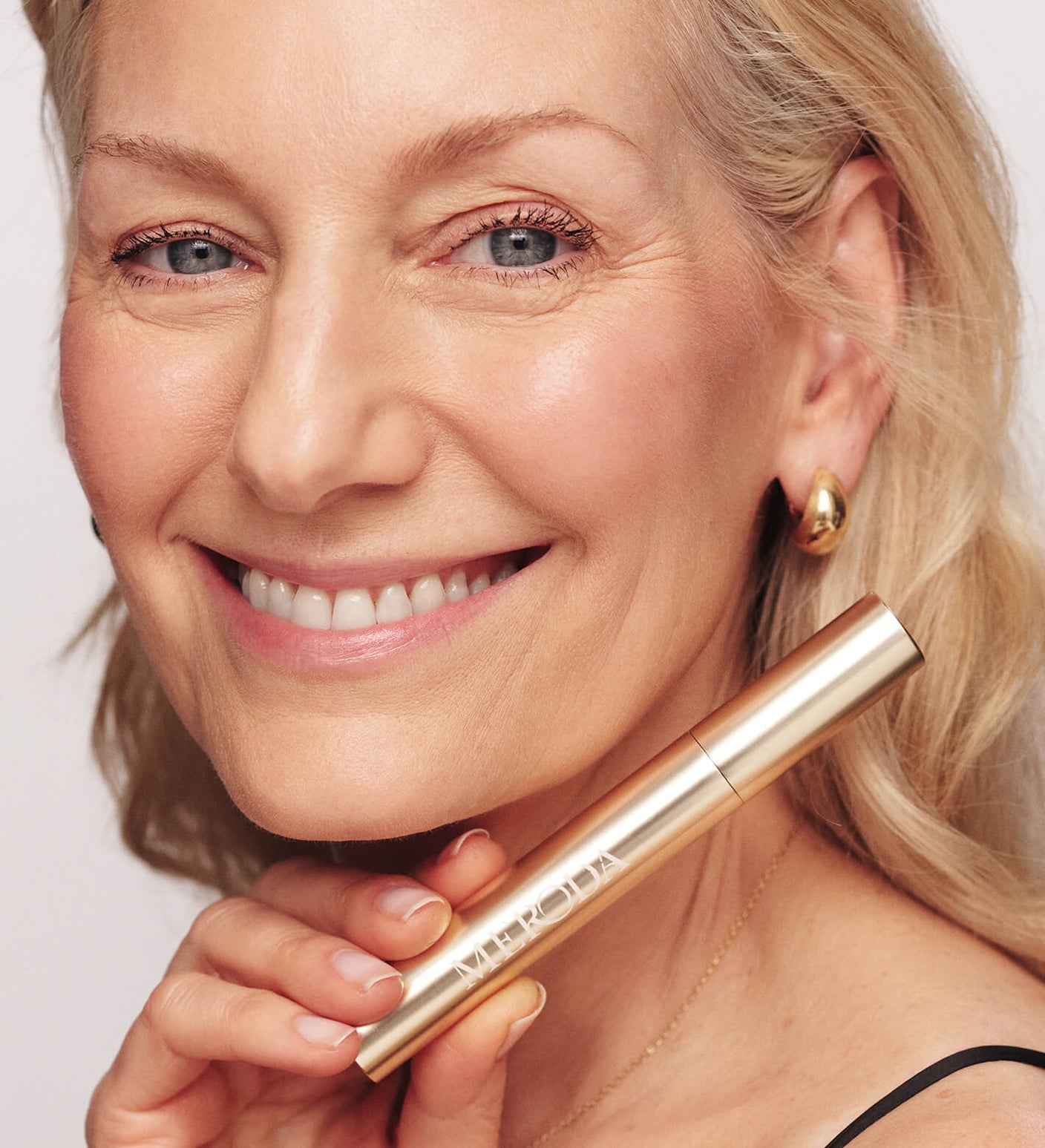 Gilded Lashes Mascara held by a smiling mature woman to showcase her lengthened and volumised lashes.